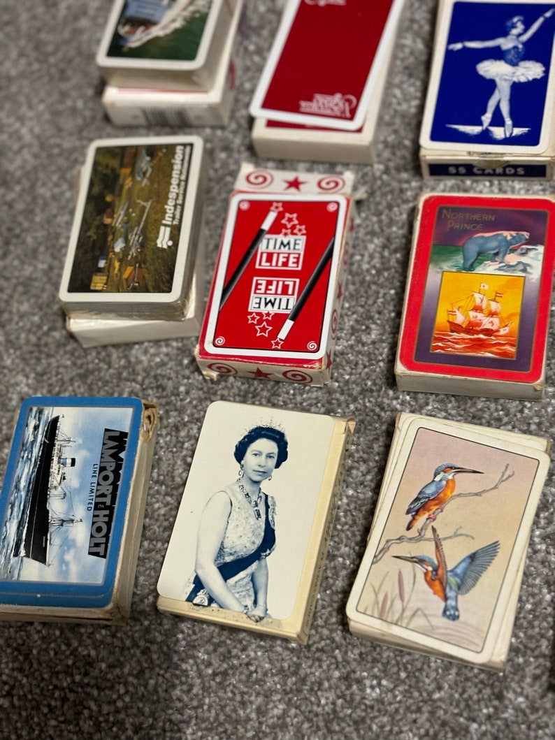May include: A collection of vintage playing cards featuring various designs. The cards include a red deck with stars and the words "Time Life", a blue deck with a ballerina, a deck with a ship and the words "Northern Prince", a deck with a queen, and a deck with a ship and the words "Import Holt Line Limited".