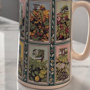 May include: A cream-colored ceramic pitcher featuring a series of rectangular panels with botanical illustrations. Each panel depicts a different plant, including Alder Buckthorn, Crab Apple, and Walnut, separated by vertical green floral borders.