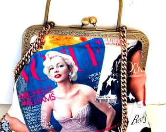 May include: A vintage-style handbag featuring a Vogue magazine cover with Michelle Williams. The bag has a gold-tone frame, handle, and chain strap. The design incorporates magazine pages, creating a unique and fashionable accessory.