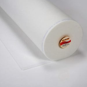 May include: A large roll of white fabric, possibly batting or interfacing, is displayed on a white surface. The roll is cylindrical, with a visible label on one end. A portion of the fabric is unrolled, lying flat.