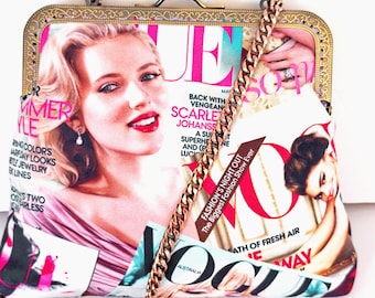 May include: A vintage-style handbag featuring a magazine cover design with a gold-tone frame and chain strap. The magazine cover features a woman's portrait and the text "Vogue". The bag has a kiss-lock closure.