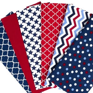 Könnte beinhalten: Eine Sammlung von sechs Stoffmustern, die fächerförmig angeordnet sind. Die Muster umfassen ein marineblaues Vierpass-Design, einfarbiges Rot, Weiß mit marineblauen Sternen, Rot mit weißem Vierpass, Zickzackstreifen in Marine, Rot und Hellblau sowie Punkte.