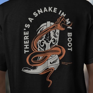 May include: Black t-shirt with a graphic design featuring a cowboy boot and a snake. The text "THERE'S A SNAKE IN MY BOOT" is arched above the boot. The snake is orange and the boot is white and orange.