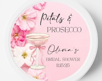 May include: A round white container with a pink label featuring a watercolor illustration of a coupe glass filled with a pink beverage, surrounded by pink flowers. The text reads Petals & PROSECCO, Olivia's BRIDAL SHOWER, and 11.15.25.