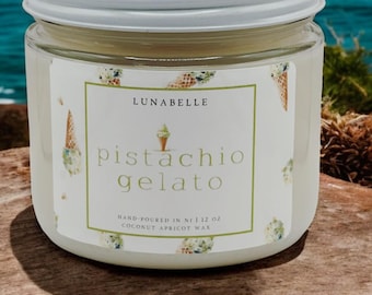 May include: A white glass jar candle with a white lid. The label reads "Lunabelle Pistachio Gelato" and "Hand-poured in NJ | 12 oz Coconut Apricot Wax".