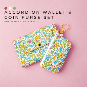 May include: An accordion wallet and coin purse set with a floral pattern in blue, yellow, and pink on a white background. The wallet has a yellow button closure, and the coin purse has a gold zipper and key ring. The text "ACCORDION WALLET & COIN PURSE SET" is at the top.