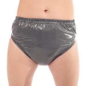 Può includere: Un paio di pantaloni di plastica grigi con elastico in vita. Il materiale lucido e impermeabile è arricciato in vita e alle aperture delle gambe. Progettato per la protezione dall'incontinenza.