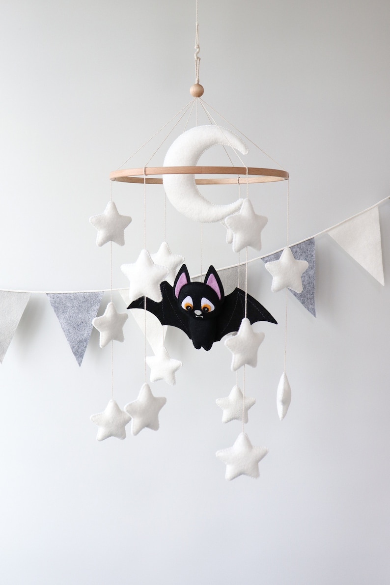 May include: A white felt moon and stars mobile with a black felt bat hanging from a wooden ring. The mobile is hanging from a white ceiling.