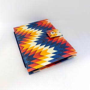 Peut inclure: Un petit portefeuille rectangulaire avec un motif géométrique coloré dans les tons de rouge, orange, jaune et bleu. Le portefeuille a une fermeture à bouton-pression et une tranche bleu foncé. Le design rappelle l'art amérindien.