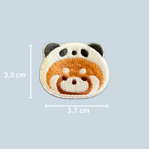 May include: An embroidered patch of a red panda wearing a panda hat. The patch measures 3.7 cm wide and 3.0 cm tall.