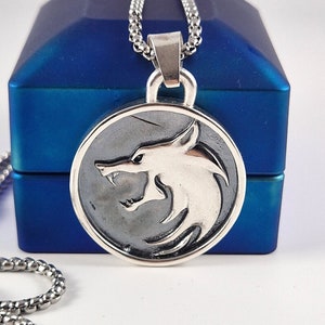 May include: A silver necklace with a round pendant featuring a wolf head design. The pendant is in a blue box.