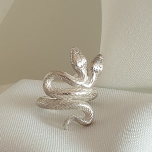 Peut inclure: Une bague en argent avec un motif de serpent à deux têtes. Le serpent est enroulé et les têtes sont tournées dans des directions opposées.