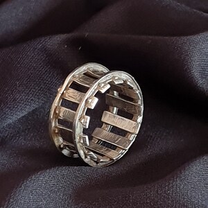 Peut inclure: Bague en argent avec un motif géométrique. La bague est composée d'une série de barres verticales reliées par une série de petits cercles.