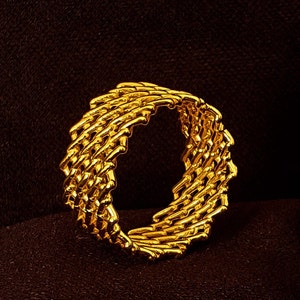 Puede incluir: Un anillo de oro con un diseño tejido. El anillo está hecho de una serie de barras de oro entrelazadas.