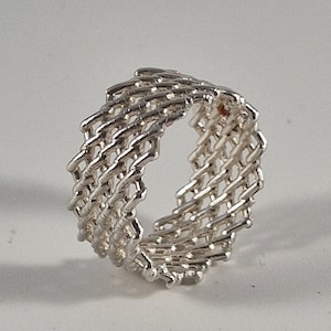 Puede incluir: Un anillo de plata con un diseño tejido. El anillo está hecho de muchas piezas pequeñas de metal interconectadas.