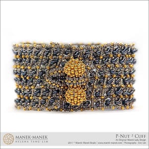 May include: A black and gold beaded bracelet with a geometric design. The bracelet is made with small, round beads and has a textured surface. The bracelet is called "P-Nut 2 Cuff" and is an original Manek Lady design.
