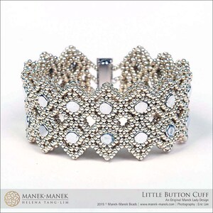 May include: A silver beaded cuff bracelet with a geometric design. The bracelet features small, round silver beads and larger, flat, circular accents. The text "LITTLE BUTTON CUFF" is visible. The bracelet is approximately 5 cm wide.