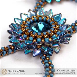 May include: A close-up of a beaded necklace with a large, blue, iridescent flower pendant. The flower is surrounded by a ring of gold beads and a smaller, blue crystal in the center. The necklace is made with blue and gold beads.