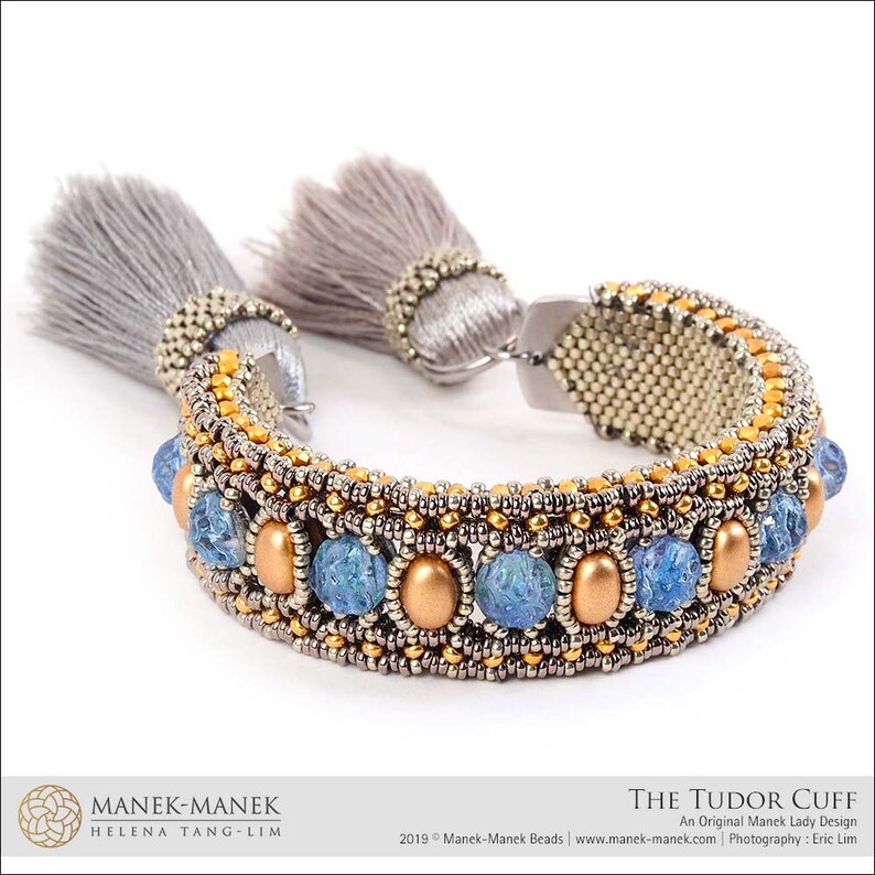 Peut inclure: Un bracelet en perles dor&eacute;es et argent&eacute;es avec des perles de verre bleues et des glands gris. Le bracelet s'appelle "The Tudor Cuff" et est un design original de Manek Lady.