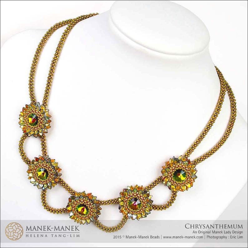 May include: A gold necklace with a double strand of beads and five flower-shaped pendants with colorful crystals. The necklace is called "Chrysanthemum" and is an original Manek Lady design.
