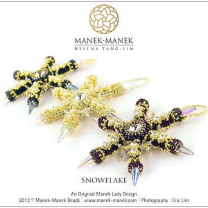 以下が含まれることがあります： 金、黒、紫のビーズでできた雪の結晶のオーナメントが3つ。オーナメントは小さなビーズで作られており、星形のデザインになっています。オーナメントの下には「SNOWFLAKE」と「An Original Manek Lady Design」の文字が印刷されています。