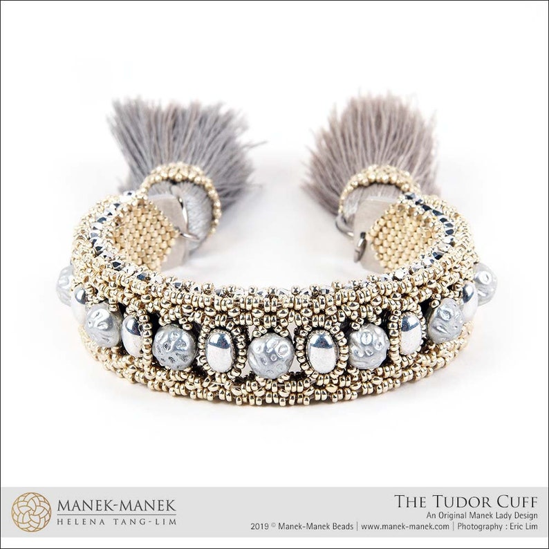 Peut inclure: Un bracelet en perles dor&eacute;es et argent&eacute;es avec un pompon en fourrure grise &agrave; chaque extr&eacute;mit&eacute;. Le bracelet s'appelle "The Tudor Cuff" et est un design original de Manek Lady.