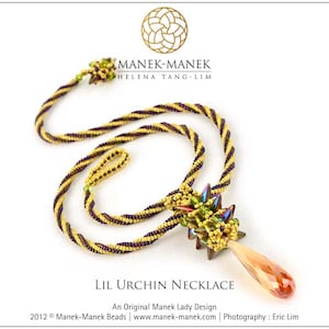 May include: A handcrafted necklace with a twisted gold and purple beaded cord. The pendant features a cluster of green and blue beads with an orange crystal teardrop. The necklace is labelled "Lil Urchin Necklace".