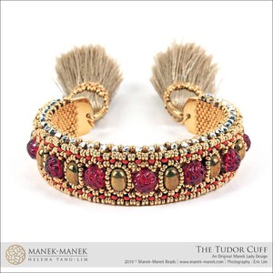 Peut inclure: Un bracelet en perles dor&eacute;es et argent&eacute;es avec des perles de verre rouges et des glands. Le bracelet s'appelle "The Tudor Cuff" et est un design original de Manek Lady.