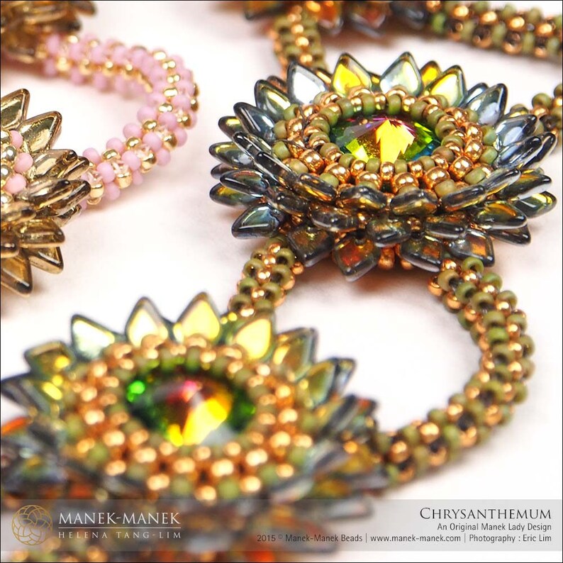 May include: A close-up of a beaded necklace with a chrysanthemum design. The necklace is made with gold, green, and iridescent beads. The beads are arranged in a flower shape with a crystal in the center.