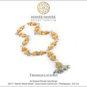 Op de afbeelding: Een gouden en zilveren ketting met een geometrisch ontwerp. De ketting is gemaakt van kleine kralen en heeft een kwast aan het einde. De ketting heet "Triangulations" en is een origineel ontwerp van Manek Lady.