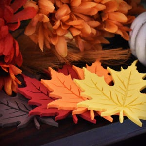 May include: A set of five fall-themed maple leaf decorations in various shades of orange, red, and yellow. The leaves are made of a soft, foam-like material and are perfect for adding a touch of autumn to your home decor.