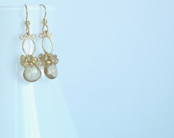 May include: Gold earrings with a teardrop-shaped gemstone and small, round beads. The earrings are made with gold wire and have a delicate, feminine design.