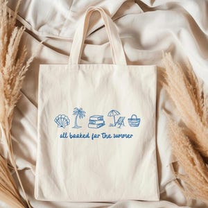 Blue outline illustration featuring a seashell, palm tree, stack of books, beach chair with umbrella, and a beach bag. Below the artwork, the phrase 'all booked for the summer' is written in playful, handwritten-style font.