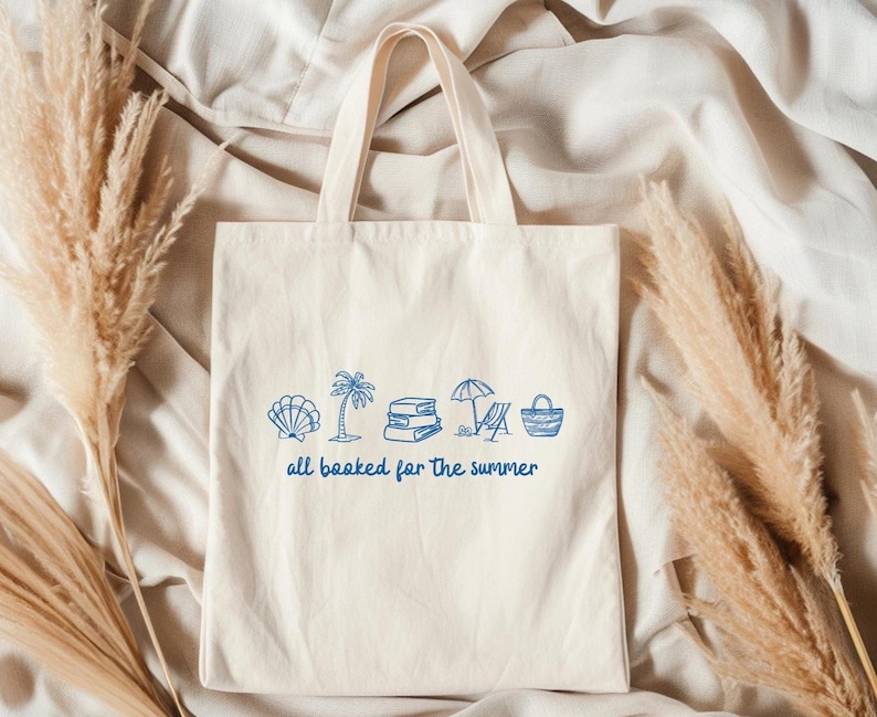 Blue outline illustration featuring a seashell, palm tree, stack of books, beach chair with umbrella, and a beach bag. Below the artwork, the phrase 'all booked for the summer' is written in playful, handwritten-style font.