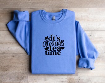 May include: A light blue sweatshirt with the phrase "it's always tea time" in black script. The design includes hearts and teacups. The sweatshirt has a crew neck and long sleeves.