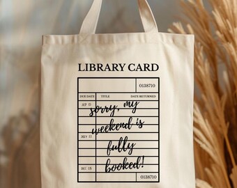 May include: Beige tote bag with black text that reads "LIBRARY CARD" and "Sorry, my weekend is fully booked!" in a library card design. The bag has two handles and is made of a canvas-like material.