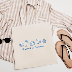 Blue outline illustration featuring a seashell, palm tree, stack of books, beach chair with umbrella, and a beach bag. Below the artwork, the phrase 'all booked for the summer' is written in playful, handwritten-style font.