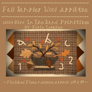 May include: A wool applique pattern featuring a basket of fall leaves, acorns, and the letters A, B, and C. The pattern is on a brown plaid fabric and measures approximately 15 inches by 9 inches.