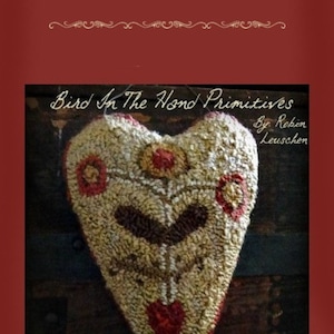May include: A beige heart-shaped rug with brown, red, and yellow details. The rug is hanging from a wooden surface. The text "Bird In The Hand Primitives" and "Colonist Punch Needle Heart Hanger #001" is visible in the image.