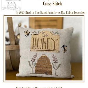 May include: A cross-stitch pillow with the words "Honey 5 Cents" and a beehive design. The pillow measures 7" x 7 1/2". The design includes bees and lavender sprigs. The text "Honey" is prominently displayed.