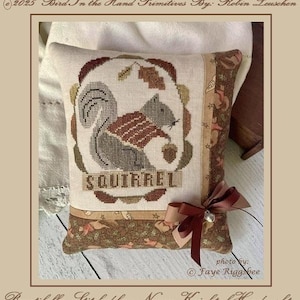 May include: A cross-stitch pillow featuring a squirrel holding an acorn, surrounded by a brown and beige border. The word "SQUIRREL" is stitched below the squirrel. The design includes the text "Sammy Squirrel & Acorn" and "Cross Stitch".