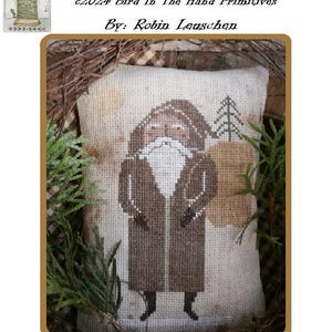 Puede incluir: Patrón de punto de cruz para un campesino de invierno, un hombre barbudo con un abrigo marrón, sosteniendo un saco y de pie frente a un árbol pequeño. La pieza terminada mide 4 pulgadas por 6 pulgadas.