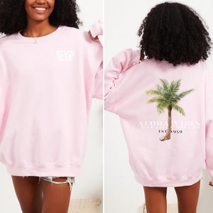 Könnte beinhalten: Rosafarbener Pullover mit "Beach Club" auf der Vorderseite und "Aloha Vibes, Hawaiian Dream, Est. 1959" und einer Palme auf der Rückseite.