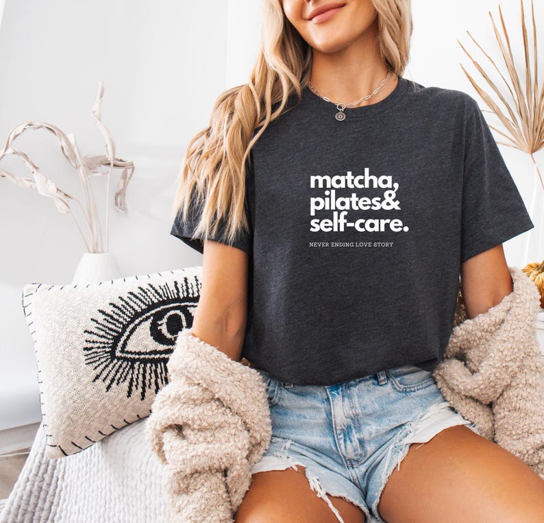 Puede incluir: Una camiseta gris oscuro con texto blanco que dice "matcha, pilates & self-care. NEVER ENDING LOVE STORY."