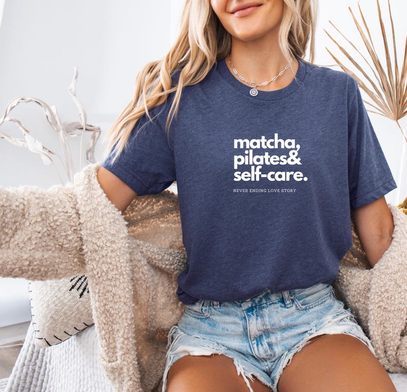Puede incluir: Una camiseta azul marino con texto blanco que dice "matcha, pilates & self-care. NEVER ENDING LOVE STORY".