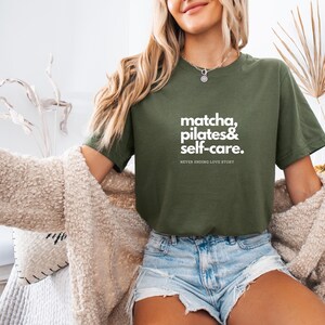 Puede incluir: Una mujer con una camiseta verde con el texto "matcha, pilates & self-care. NEVER ENDING LOVE STORY" en letras blancas.