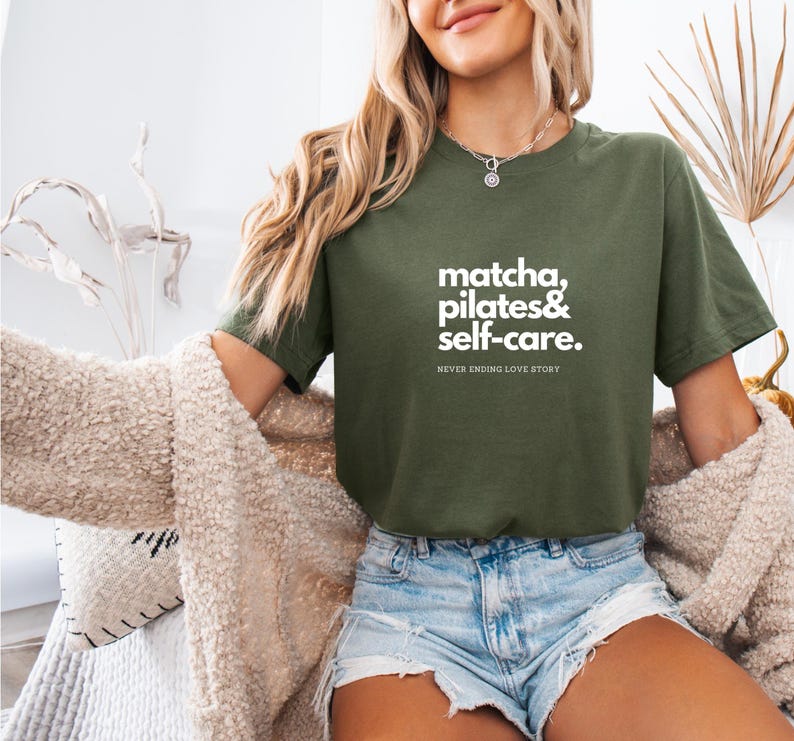 Puede incluir: Una mujer con una camiseta verde con el texto "matcha, pilates & self-care. NEVER ENDING LOVE STORY" en letras blancas.