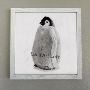 May include: A square framed wall art piece featuring a black and white pencil sketch of a fluffy penguin chick. The drawing is centred on a white background within a textured white wooden frame. The text Luca Art Loft is printed in grey.