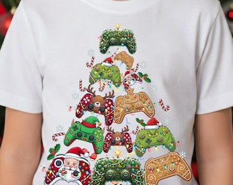 May include: White t-shirt featuring a Christmas tree design made of decorated game controllers. The controllers are adorned with Santa hats, gingerbread men, and festive lights. A red gift box is at the base of the tree.