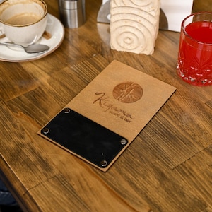 May include: A brown leather menu with a black insert and the text "Kiyam" in a stylized font. The menu has a circle with a bamboo design and the words "Restaurant & Bar".